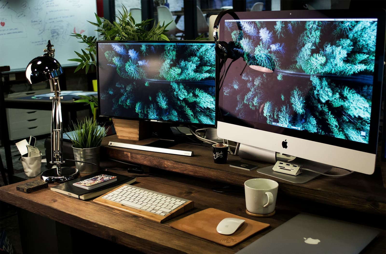 Two monitors, keyboard and desk lamp on a wooden desk